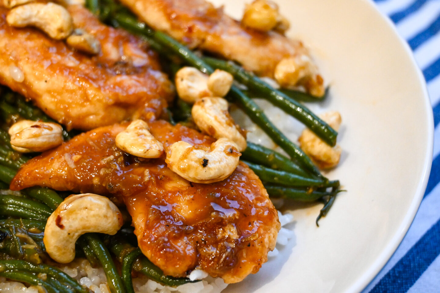 Chicken Mini Fillets glazed in a honey & garlic sauce on a bed of sticky white rice with green beans and cashews closeup