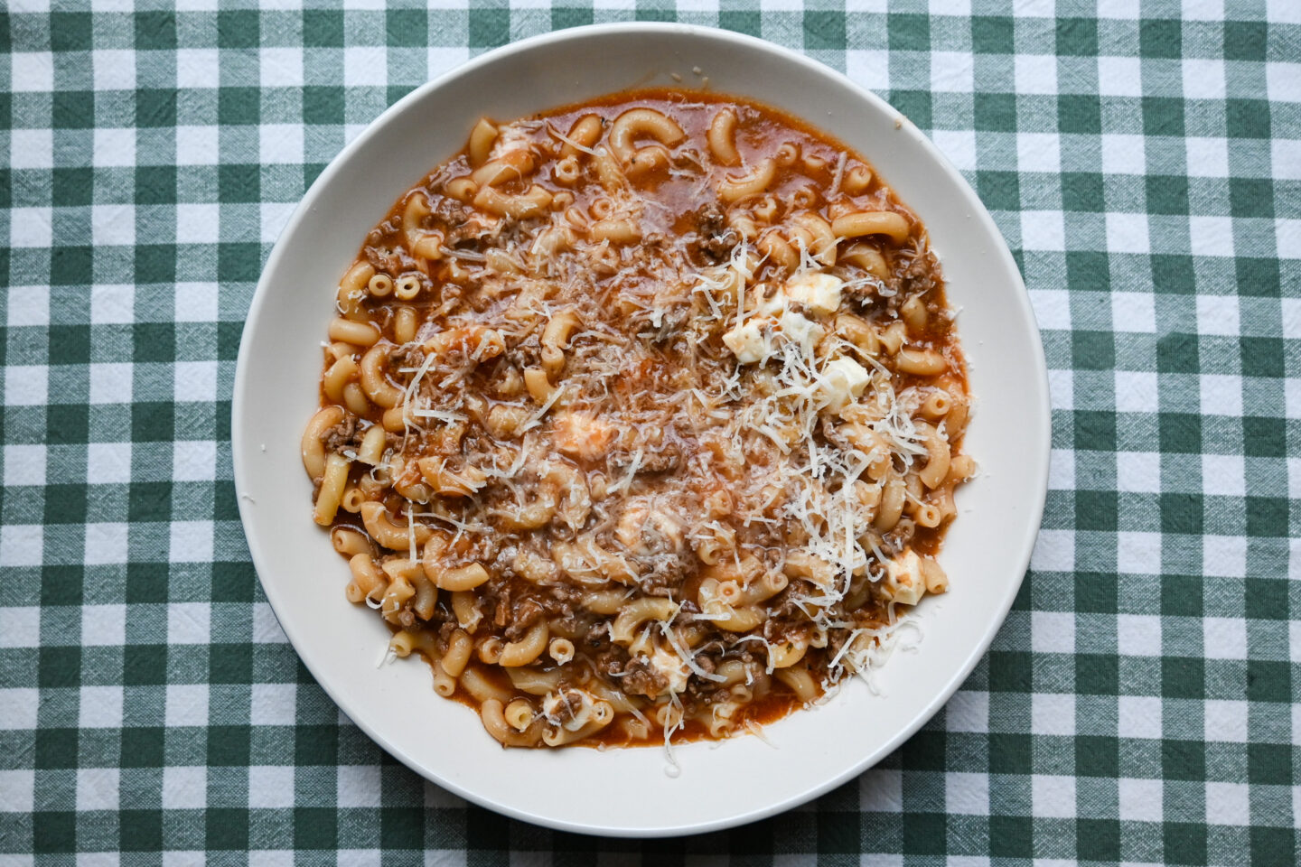 Bowl of Cheesy Beef-a-Roni sprinkled with Parmesan cheese on a green & white background