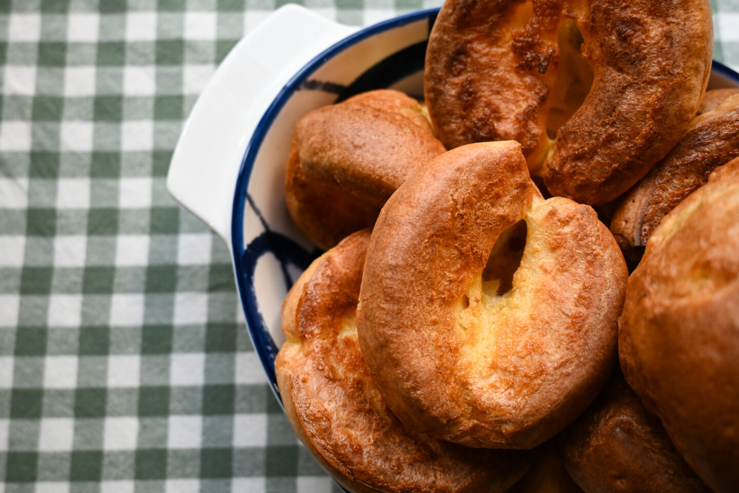 Miniature Yorkshire Puddings in a blue & white porcelain serving dish on a green & white gingham background