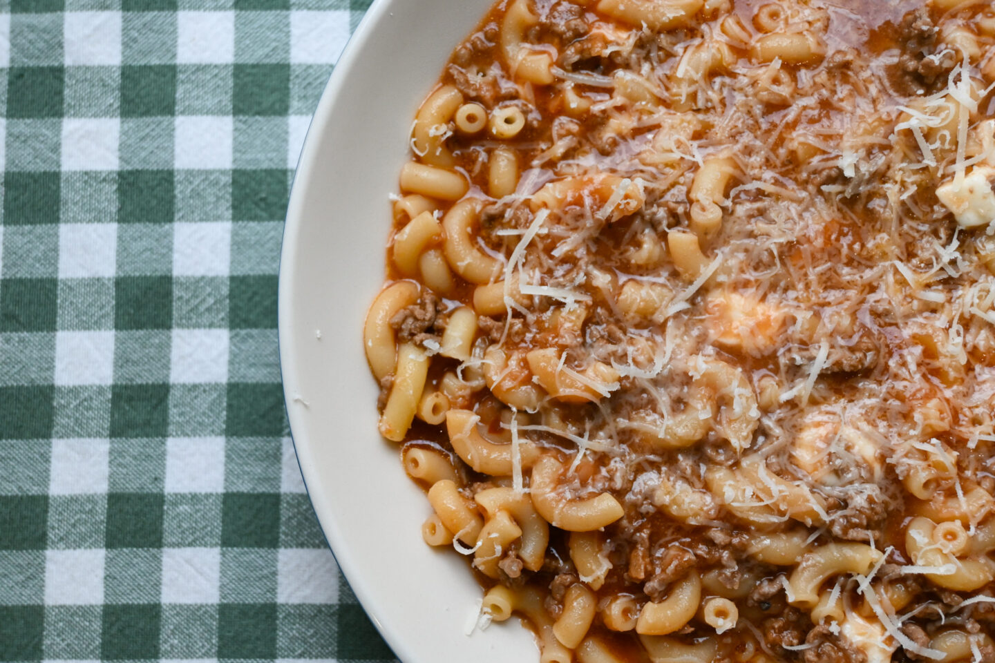 Bowl of Cheesy Beef-a-Roni sprinkled with Parmesan cheese on a green & white background