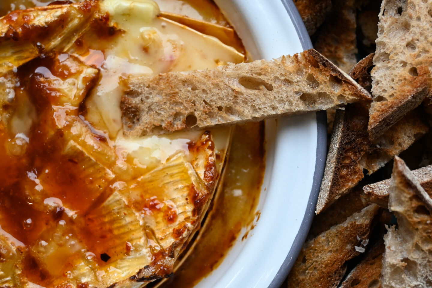 Closeup of Harissa Honey Baked Camembert with toasted sourdough bread dipped into the melted cheese