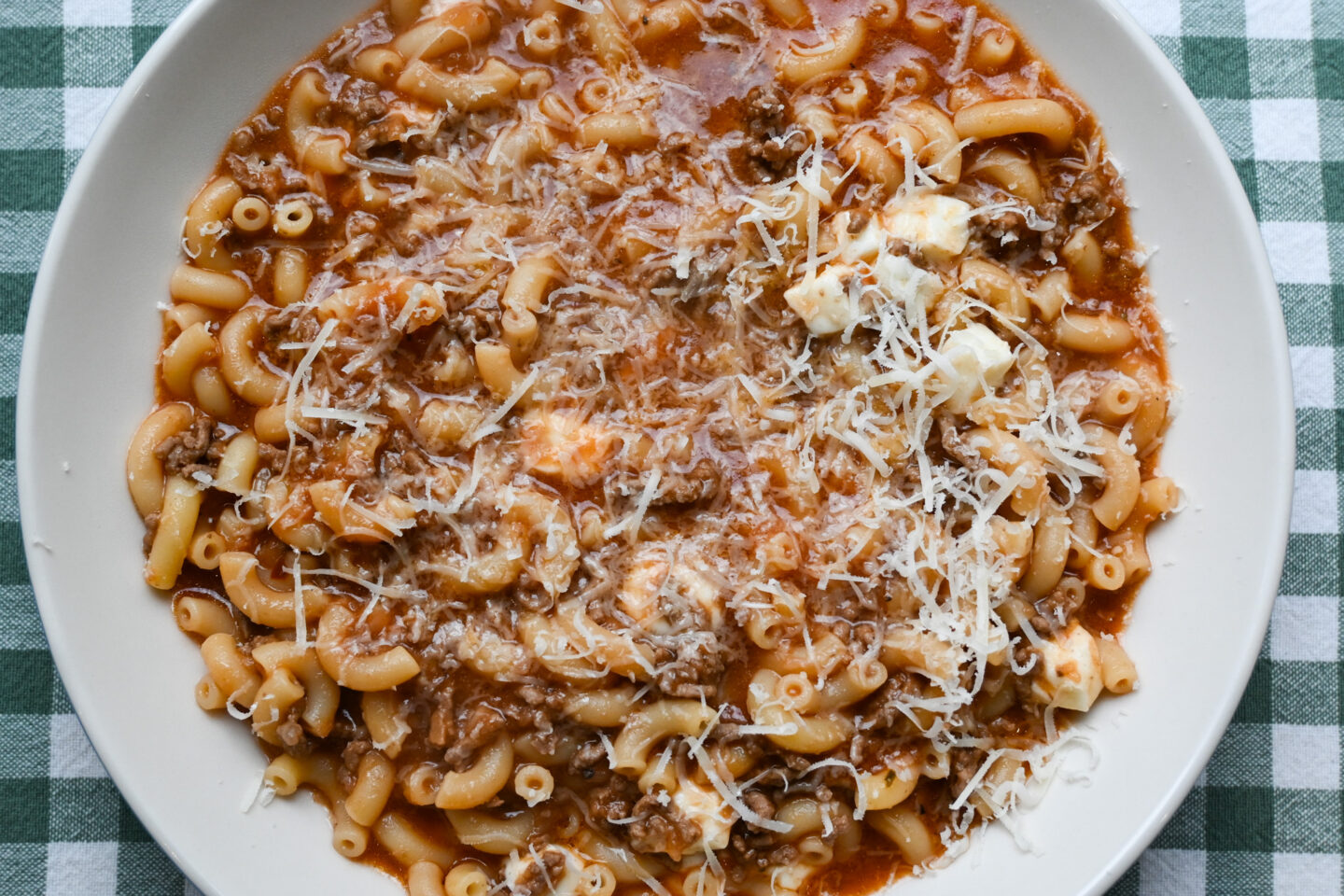 Bowl of Cheesy Beef-a-Roni sprinkled with Parmesan cheese on a green & white background closeup