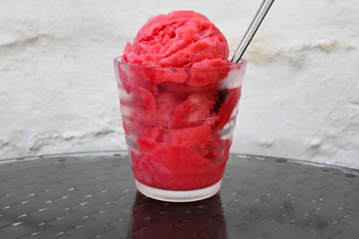 3 scoops of Raspberry Sorbet in a glass with a spoon on a black table with a white background